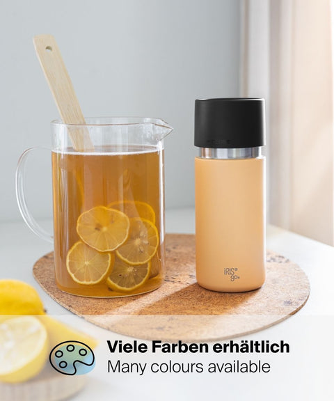 IRISgo® cup flow 500ml Thermobecher in vibrant orange neben einer Kanne Eistee mit Zitronen, erhältlich in vielen Farben