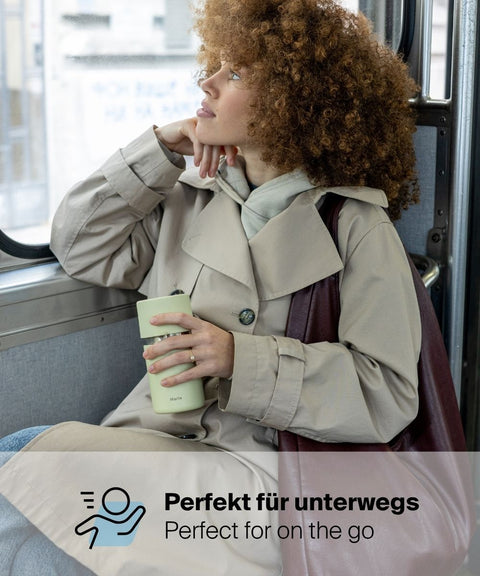 Frau im Mantel hält den IRISgo® cup sip 350ml Thermobecher in vanilla cream im Bus, perfekt für unterwegs