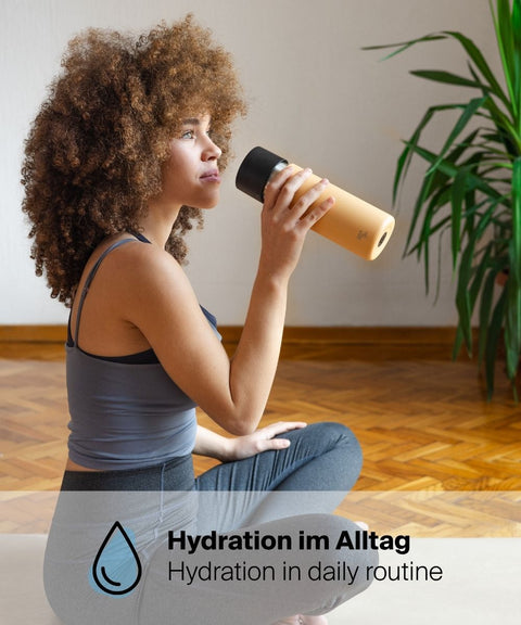 Frau trinkt im Schneidersitz aus dem IRISgo® cup stream 650ml Thermobecher in vibrant orange, Hydration im Alltag